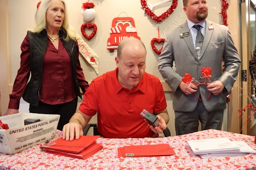 Governor Polis sitting at a table stamping valentines Day letters in Loveland Colorado