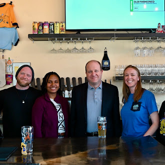 Governor Polis Stands for photo at Novel Strand Brewing Co.