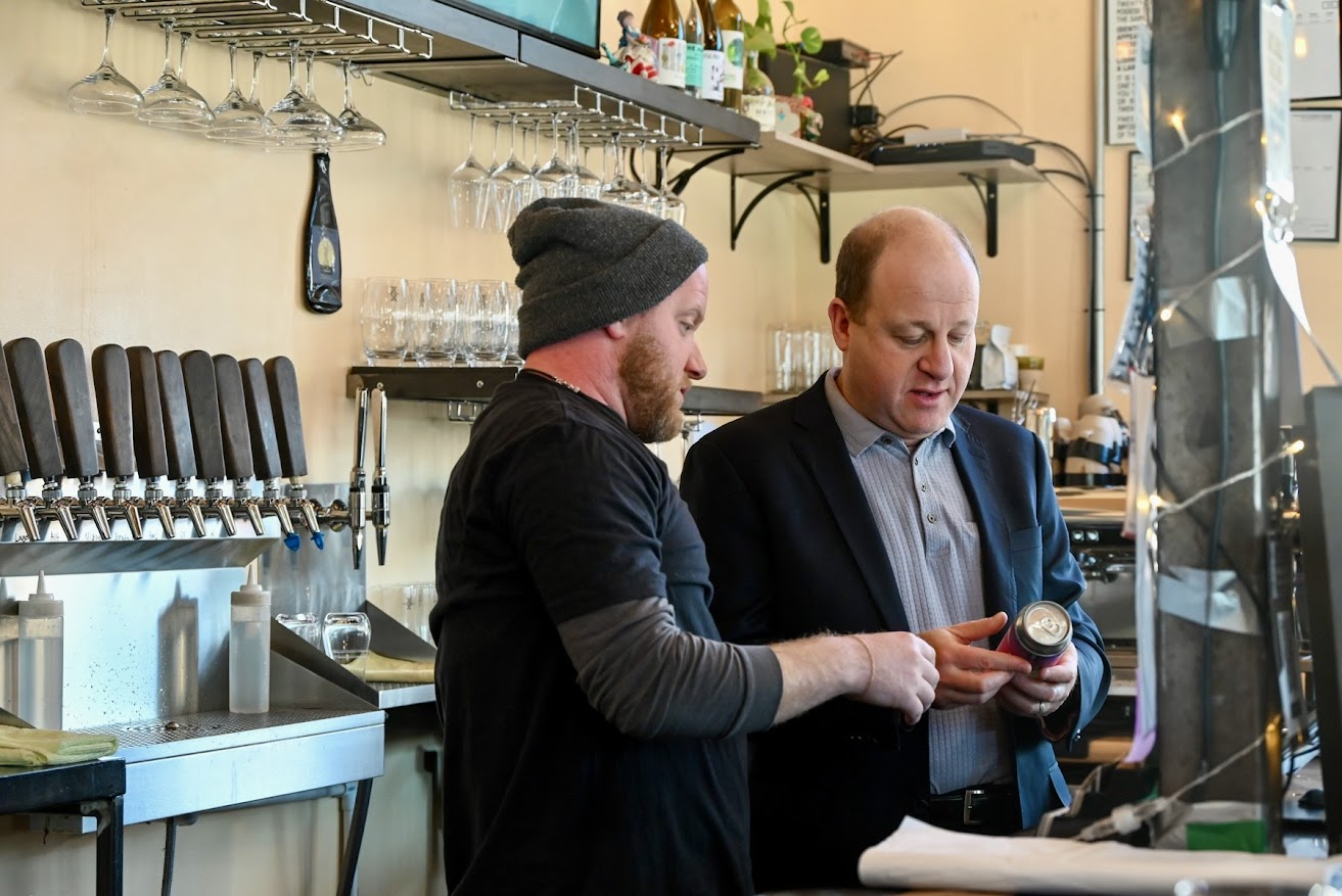 Governor Polis checks out the label on Novel Strand Brewing Co. can