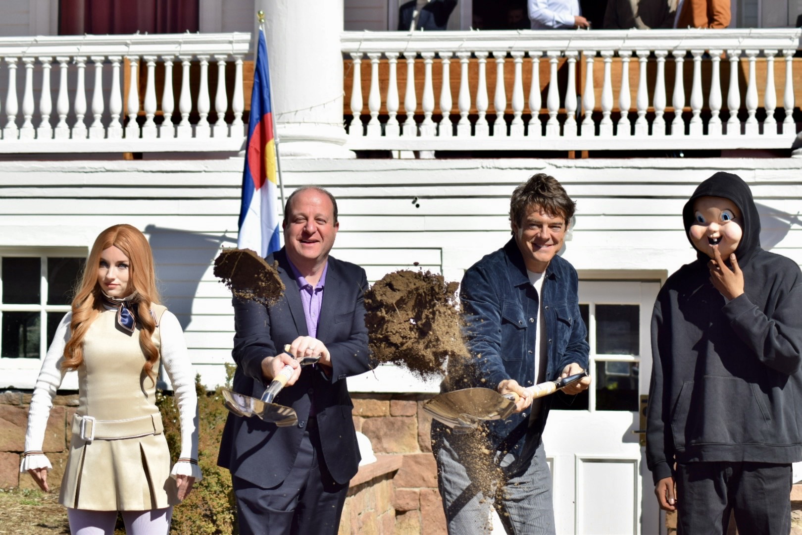 Governor Polis and Blumhouse CEO Jason Blum throw dirt with shovels during the groundbreaking Ceremony of the Stanley Exhibit Center. The pair are flanked by characters from Blumhouse movies "Megan" and "The Purge". 
