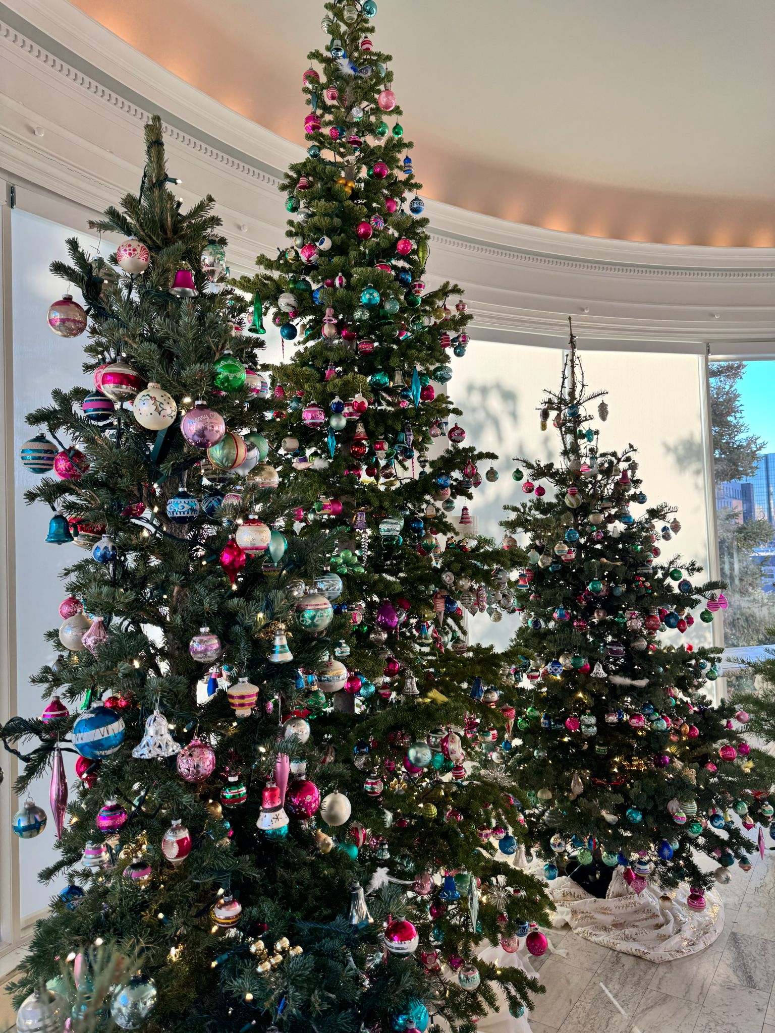 Three christmas trees decorated in bright ornaments in the palm room.