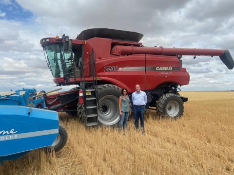 Governor Polis stands with woman in front of large harvester.