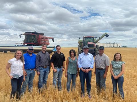 Governor Polis poses with others in field with farm equipment.