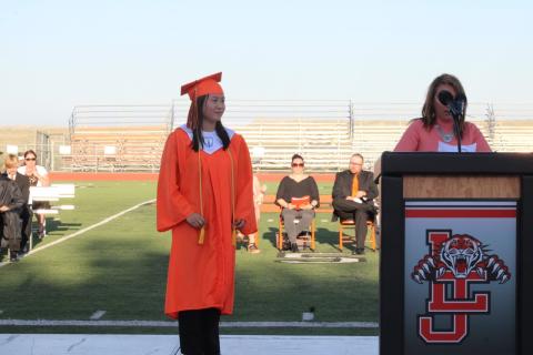 La Junta High School student Shealie Schmidt in an orange cap and gown next to the podium.